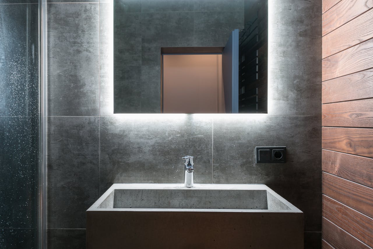 Sleek modern bathroom featuring an illuminated mirror, concrete sink, and elegant gray tiles.